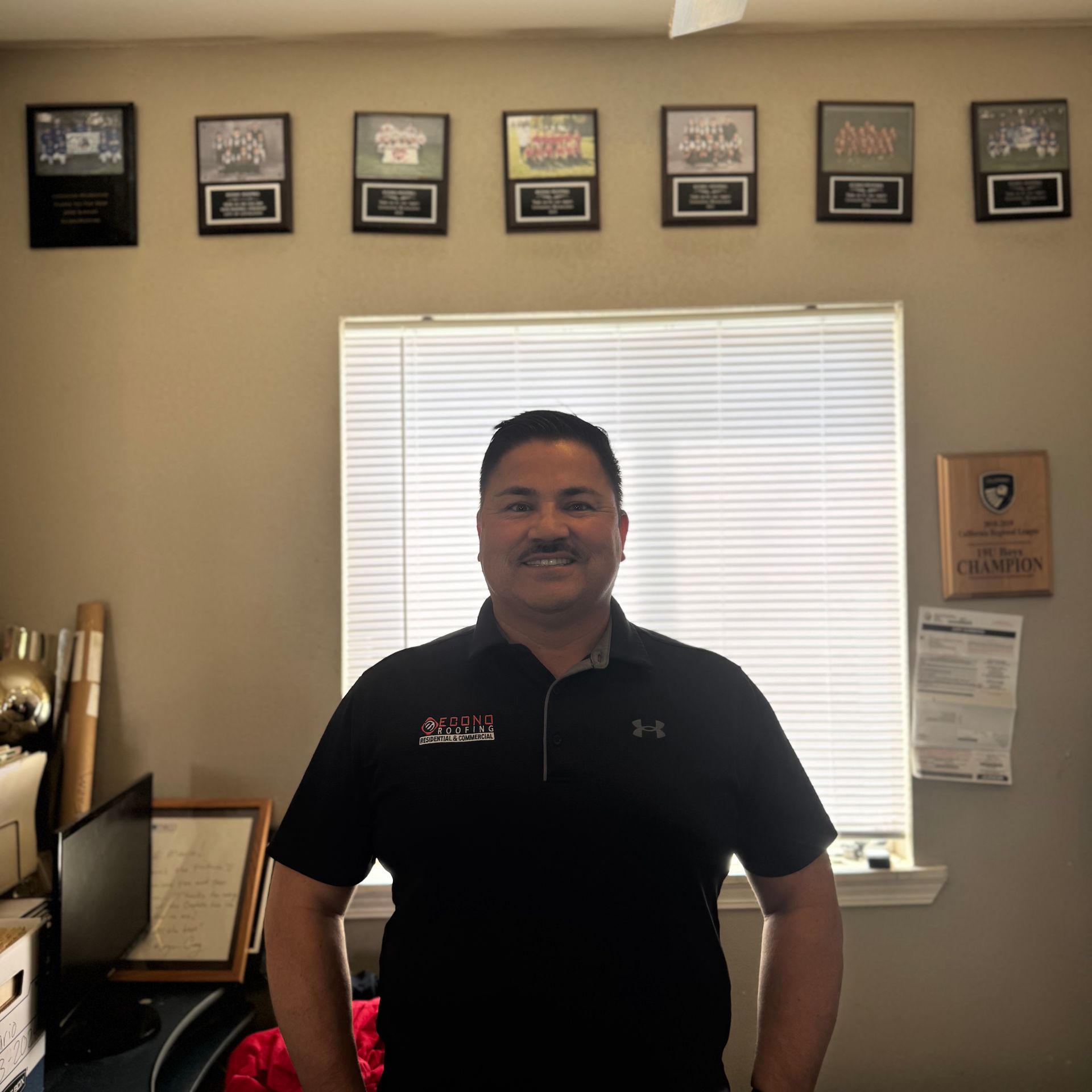 A man is standing in front of a window with plaques on the wall behind him