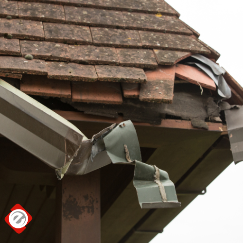 Damaged roof with missing tiles and bent green guttering.