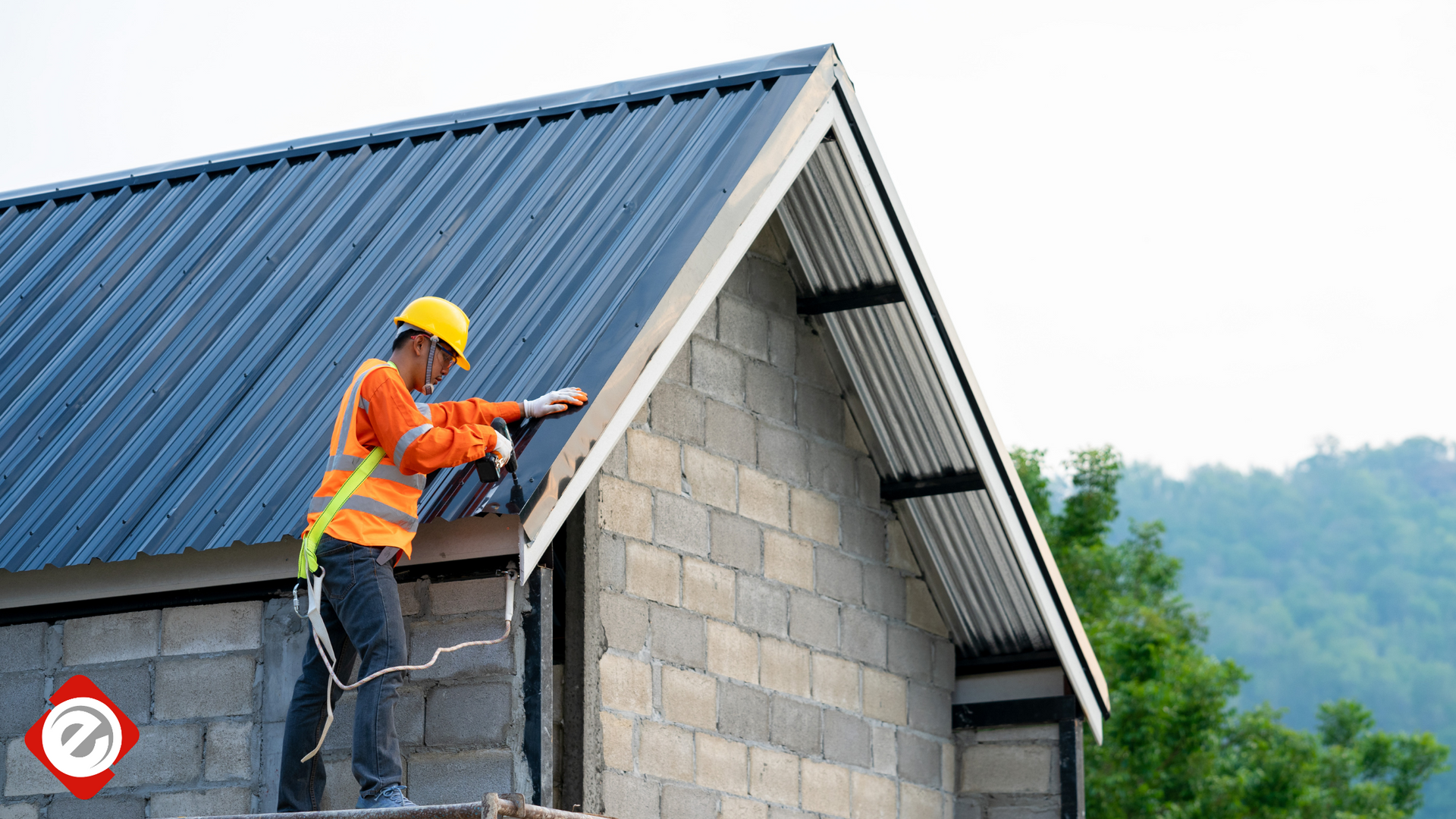 Construction worker in safety gear installing a blue metal roof on a cinder block building.
