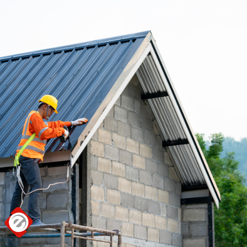 Construction worker in safety gear installing a metal roof on a cinder block building.
