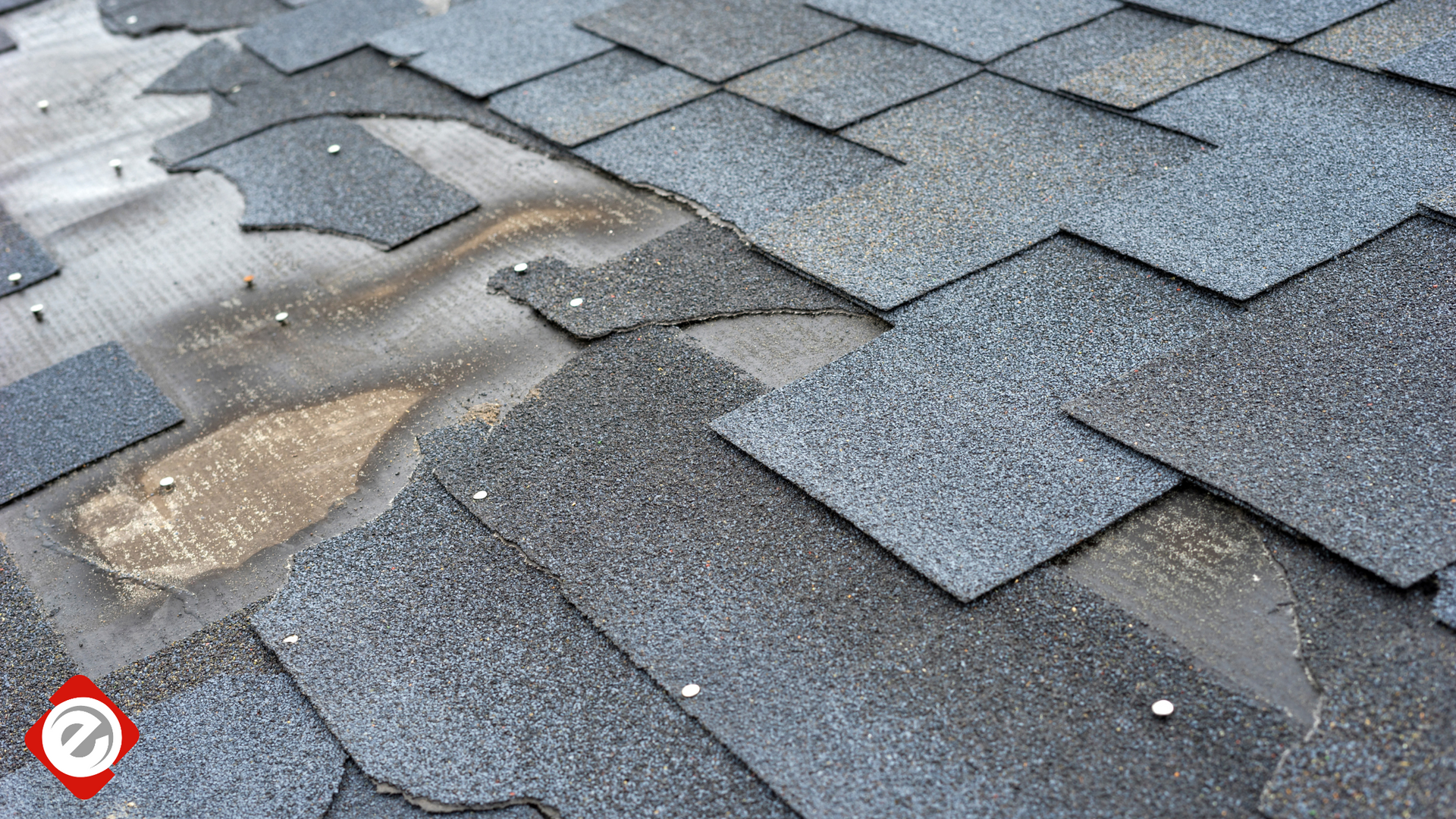 Damaged asphalt shingles on a roof, showing missing and worn patches.