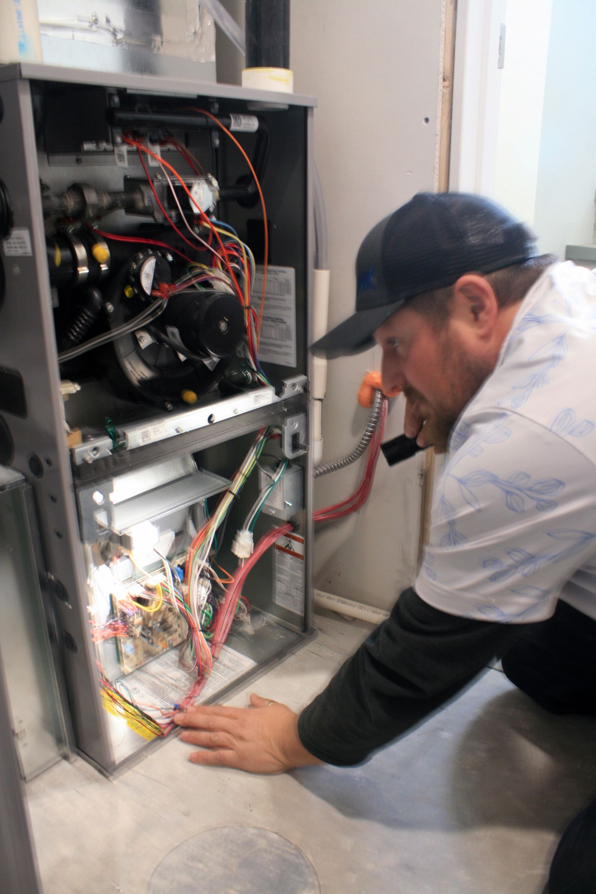 Technician kneeling beside an open electrical cabinet, inspecting wiring with tools in a utility room