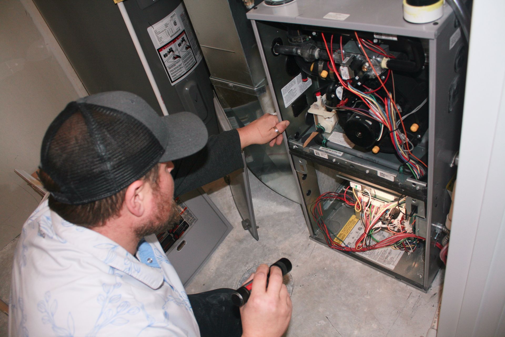 A man is working on an air conditioner with a flashlight.