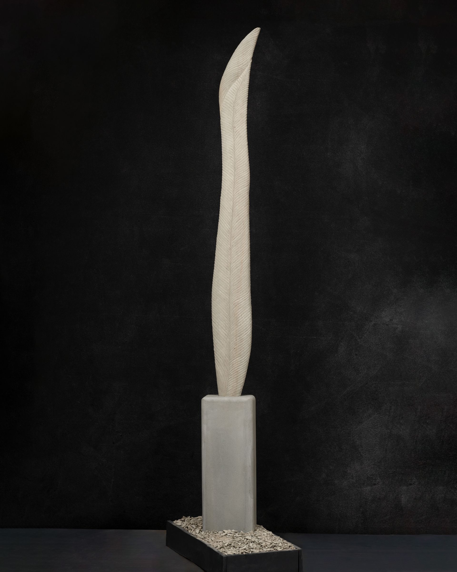 A white sculpture is sitting on top of a white block on a black background.