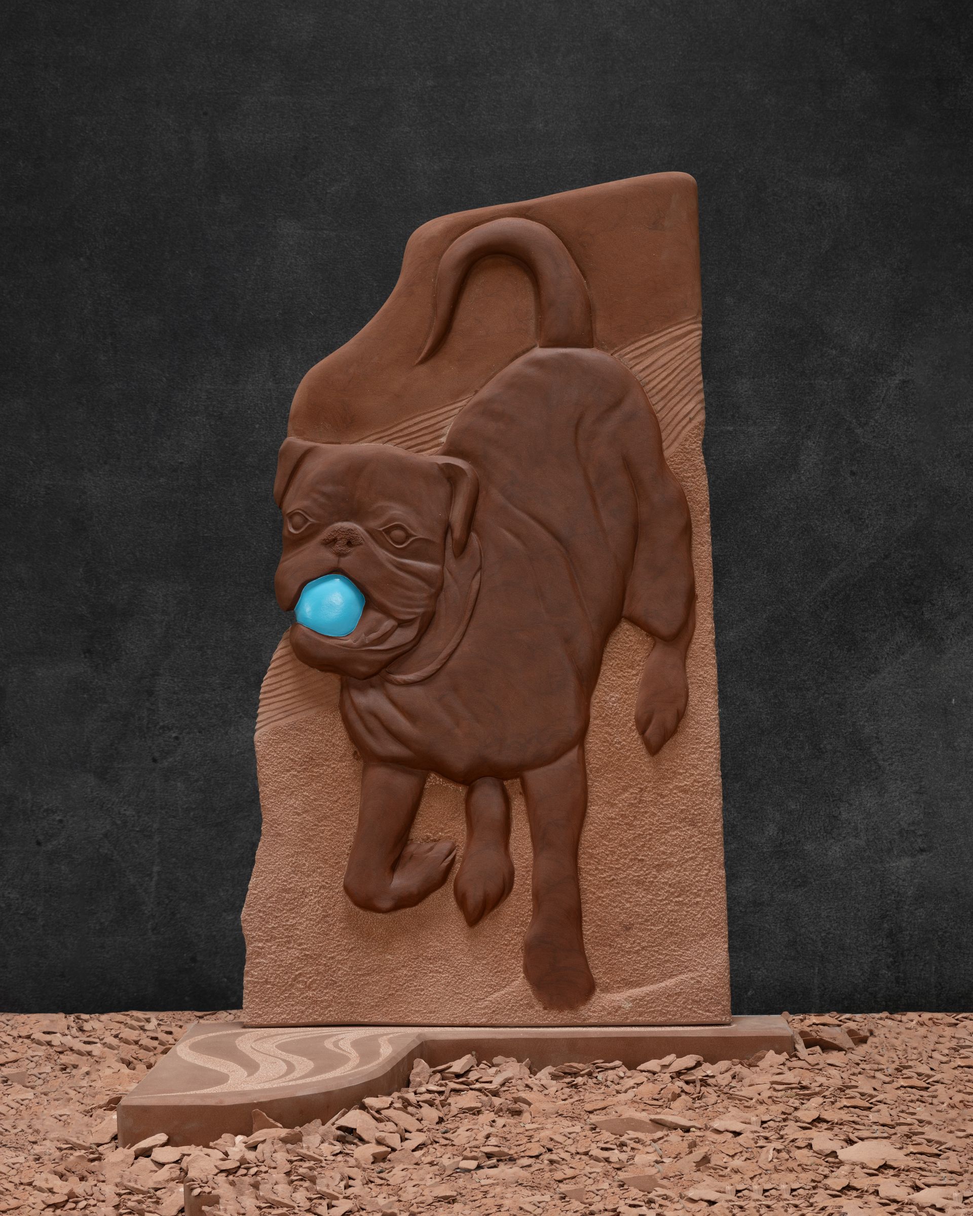 A statue of a pug dog with a blue ball in its mouth
