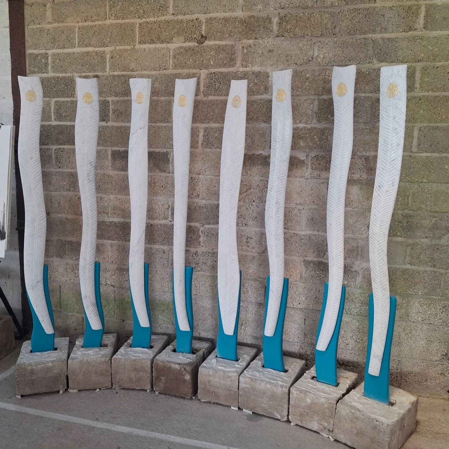 Row of tall white-and-blue sculptures on concrete bases against a brick wall