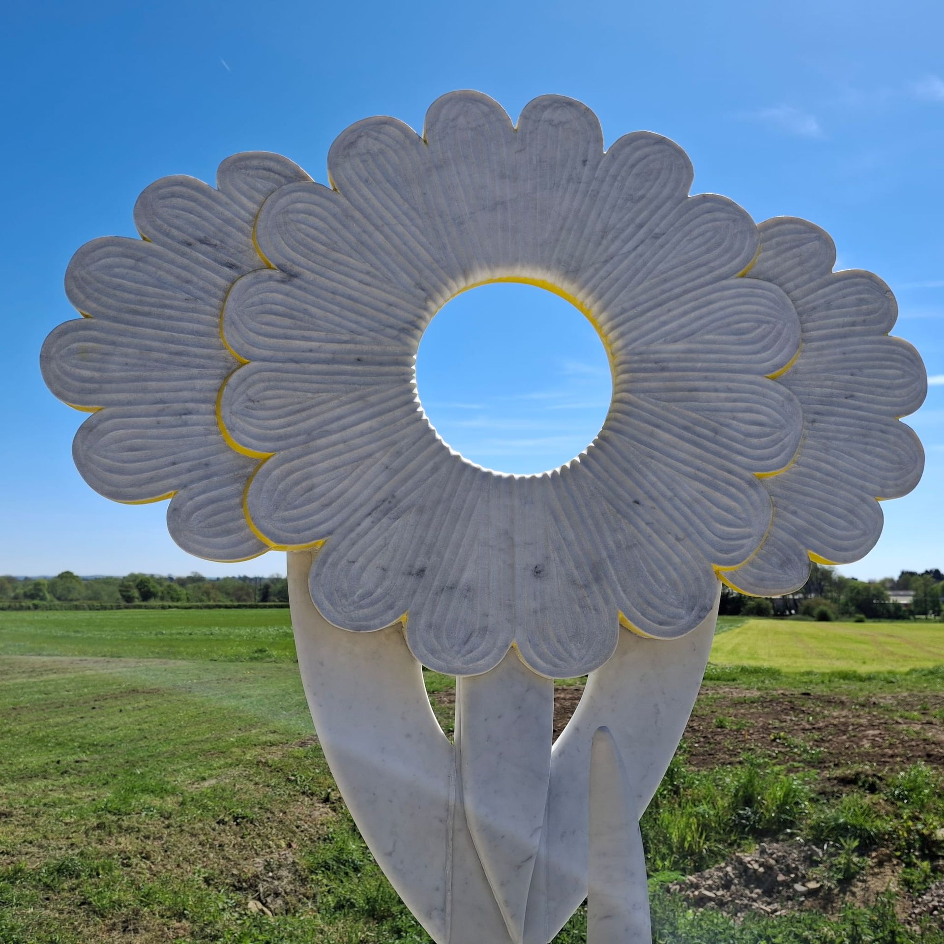 White flower-shaped sculpture in a grassy field under a blue sky