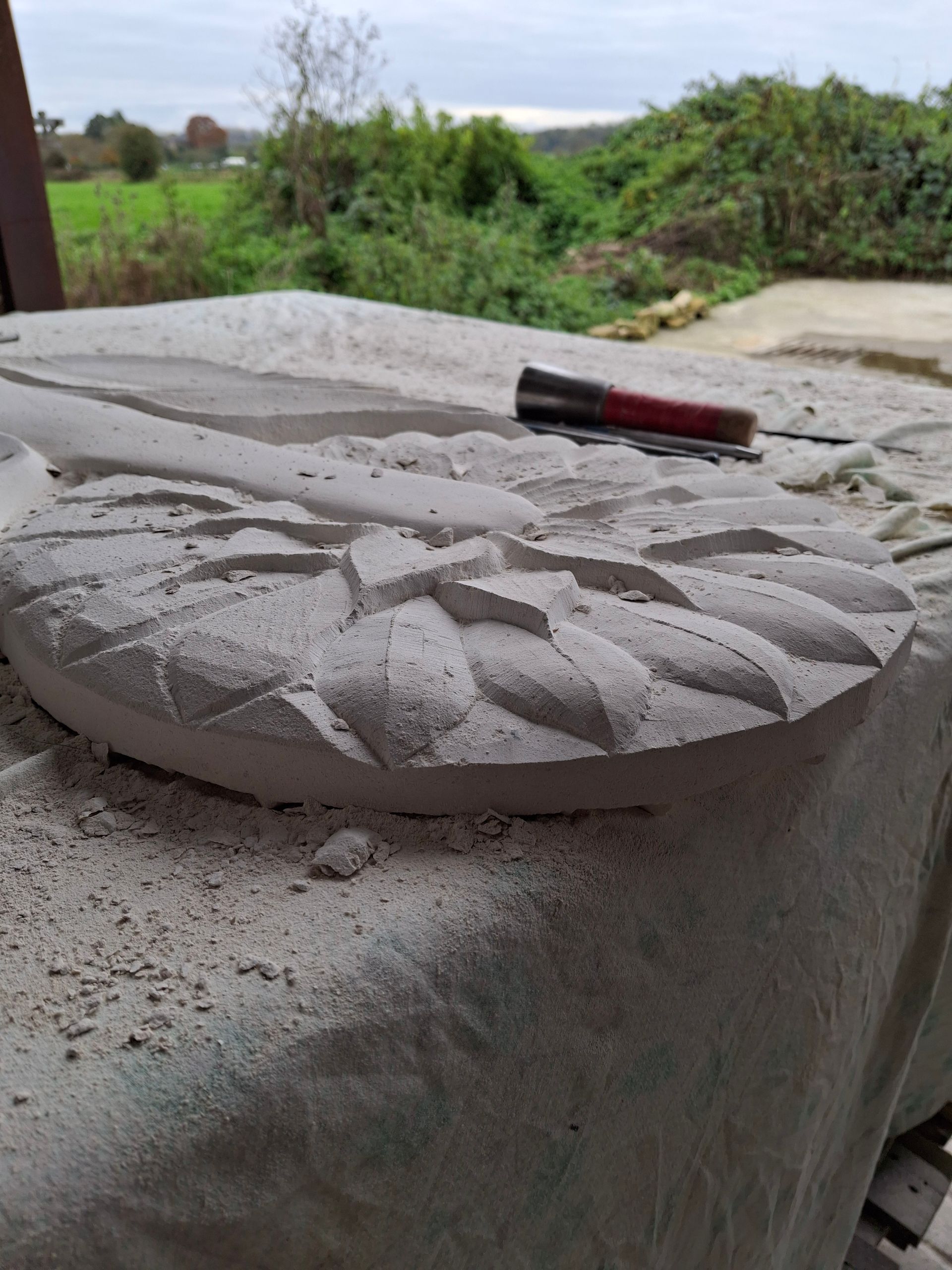 Circular concrete disc on a rough ledge with a red-and-black tool, outdoors near greenery