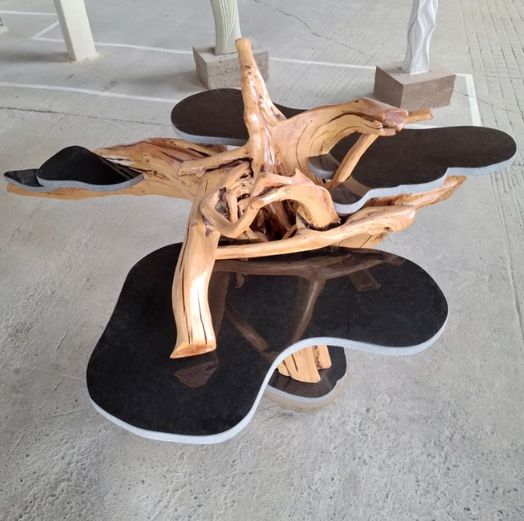Abstract wooden sculpture on black petal-shaped base in a concrete outdoor setting