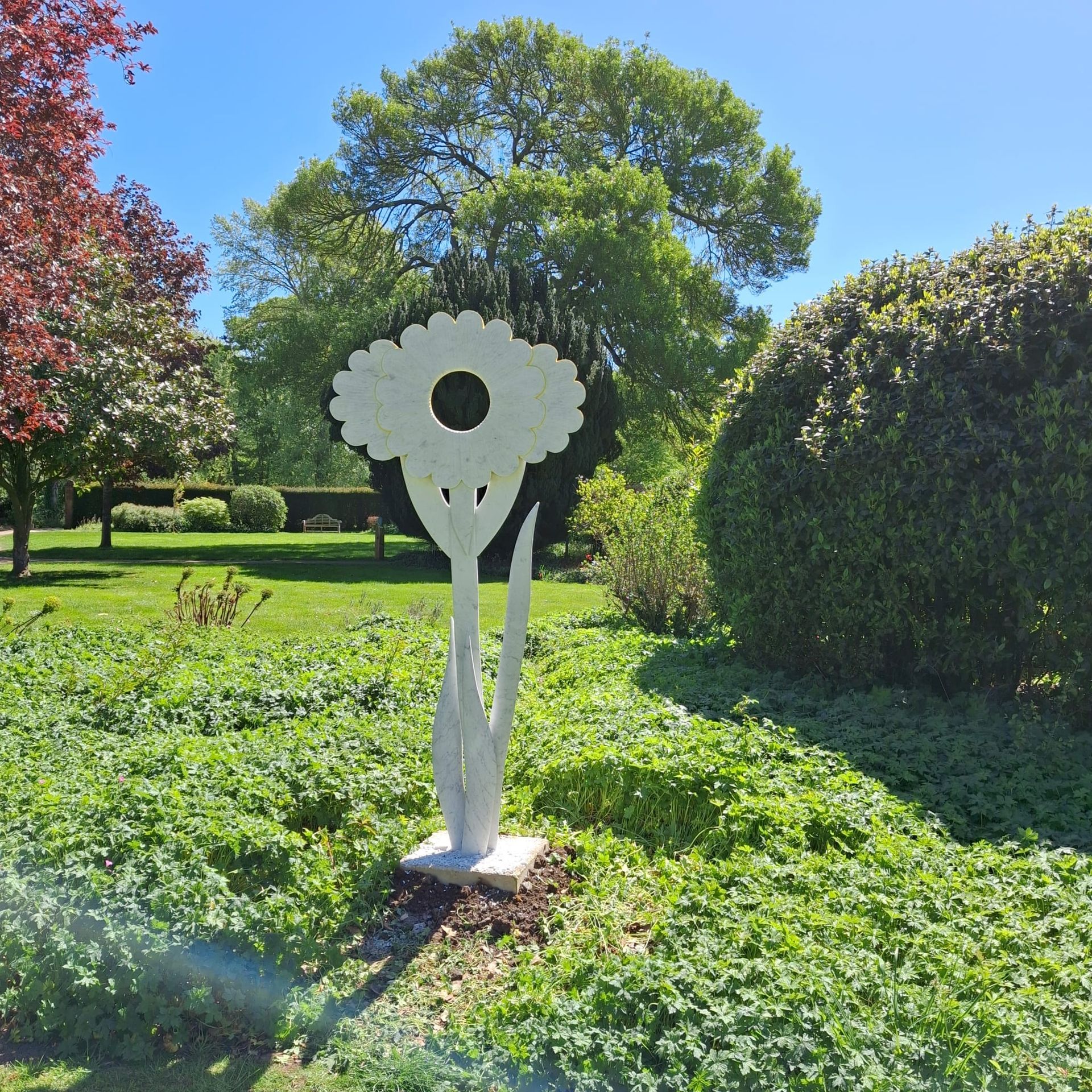 White flower sculpture in a sunny green garden with trees and shrubs