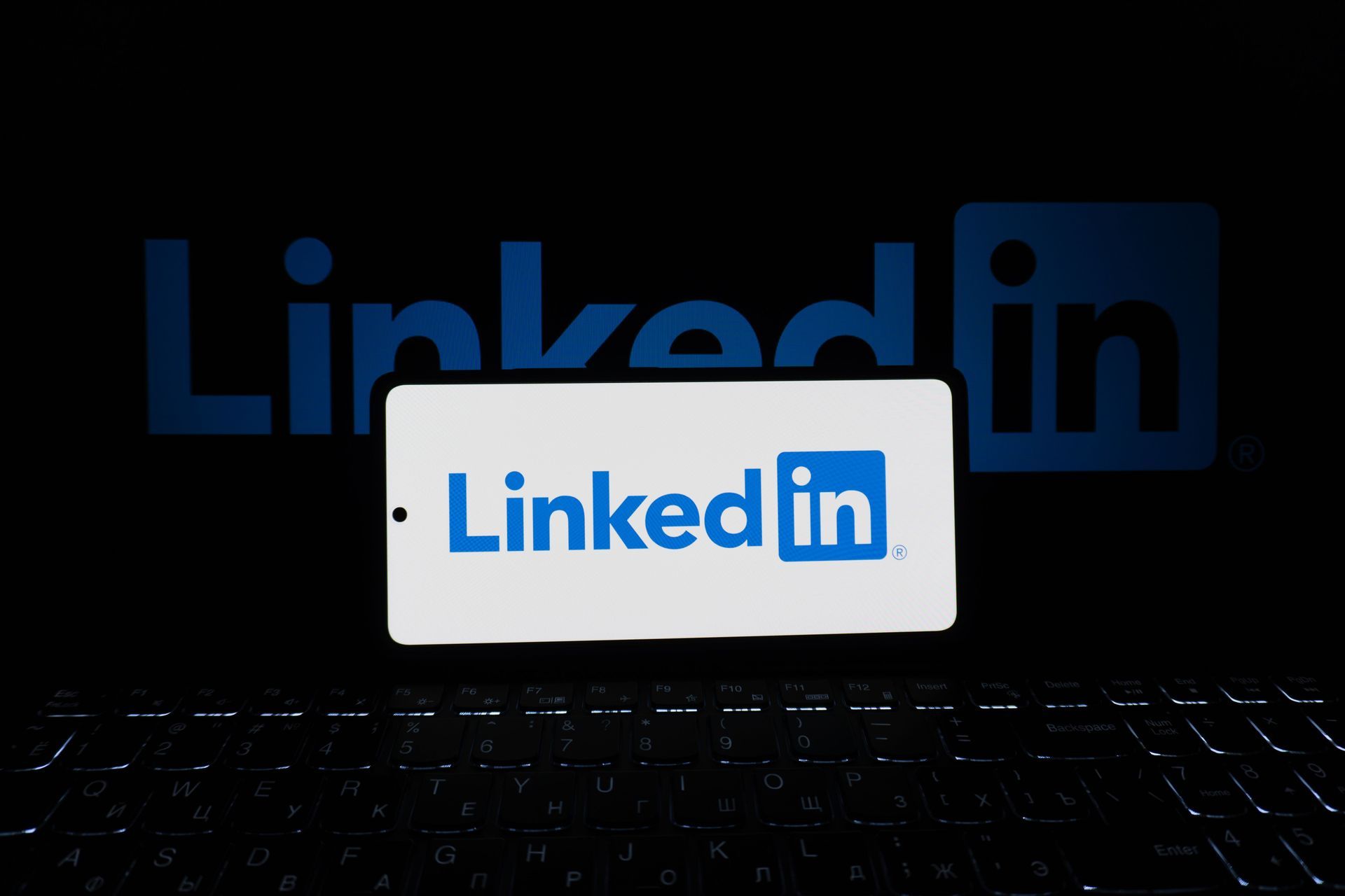 LinkedIn on a phone in front of a screen with the big LinkedIn logo