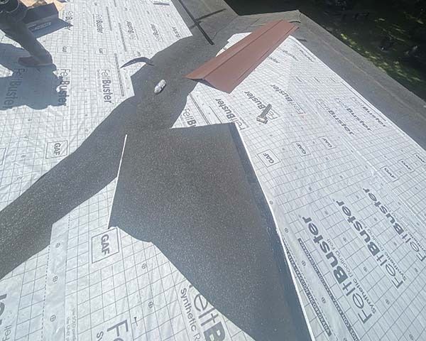 Roof underlayment with dark shingles and wooden planks on a sloped rooftop in sunlight