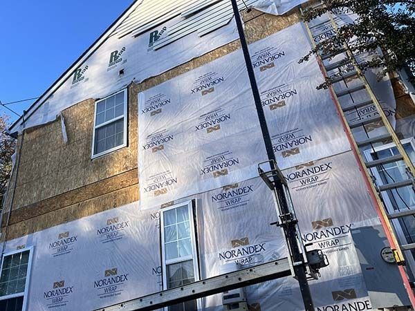 House exterior under construction with silver insulation wrap, windows, and a ladder against the wall.