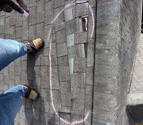 Worker’s boots on a gray shingled roof, marking and measuring with pink chalk lines.