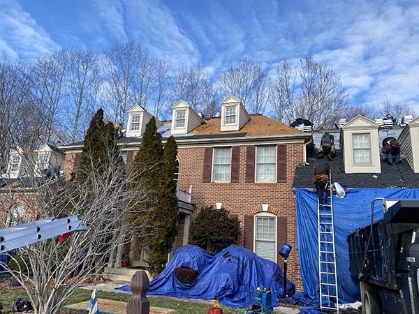 Brick townhouse with ladders, blue tarps, and workers on the roof and in the yard