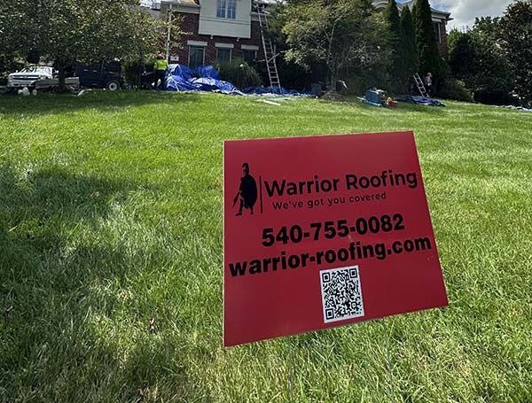 Red Warrior Roofing yard sign on a grassy lawn with phone number and website.