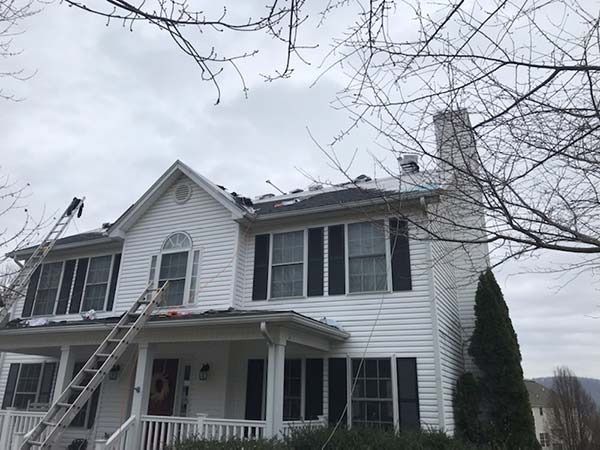 Two-story white house with a ladder on the front and roof, under an overcast sky