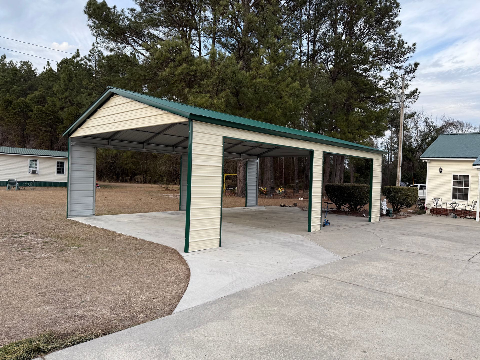 Open-sided carport with green trim beside a gravel driveway and mobile homes