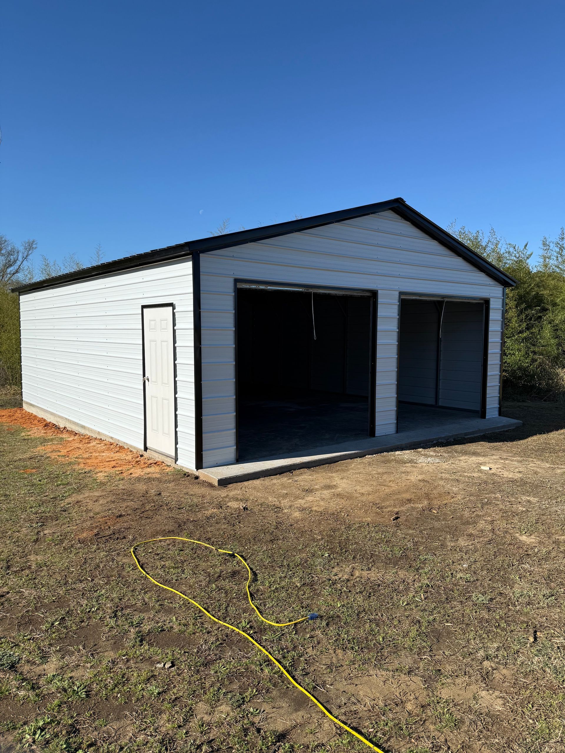 White two-bay garage with open doors on a grassy lot under a clear blue sky
