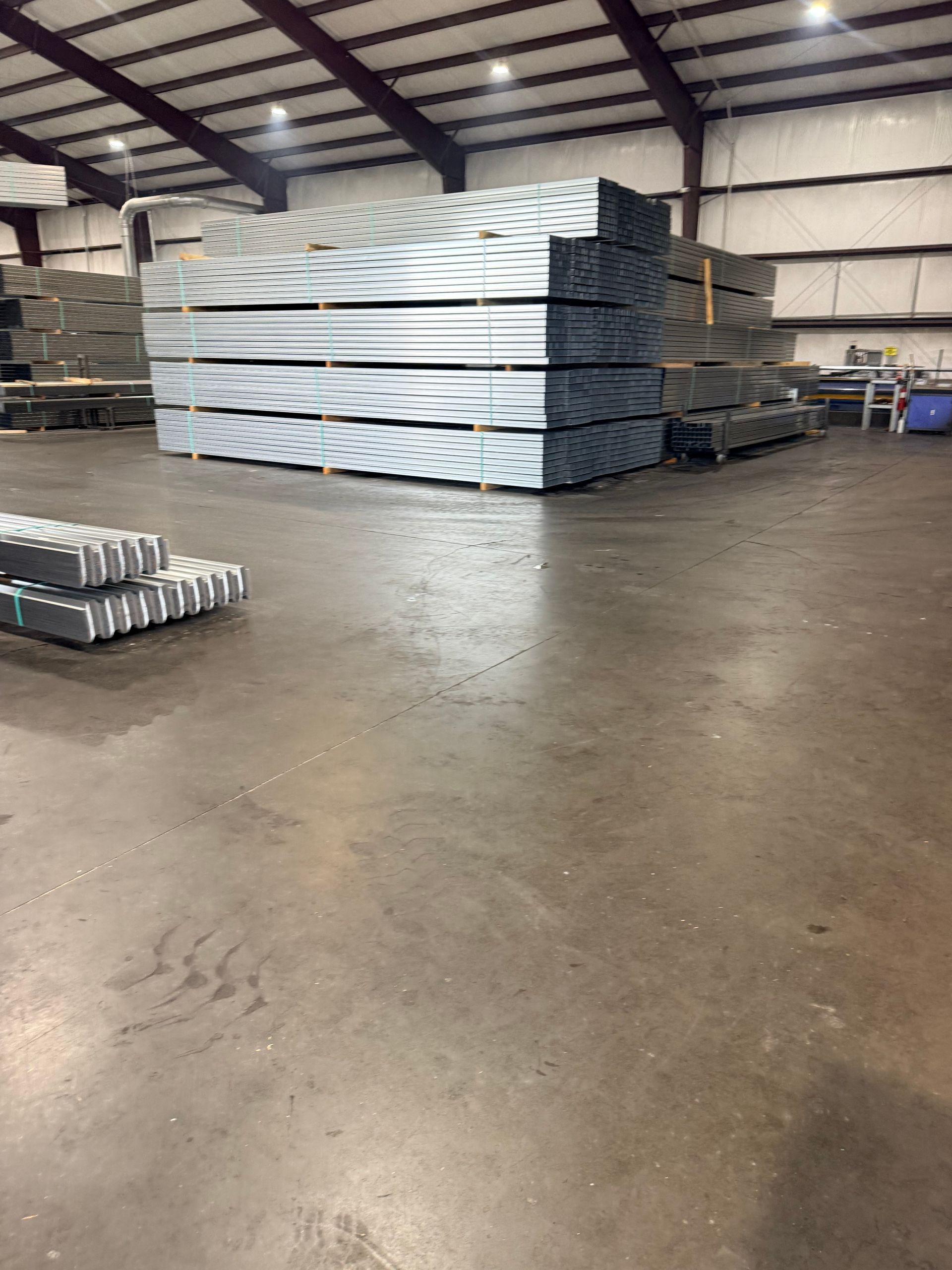 Stacked white metal panels in a warehouse with a concrete floor and industrial ceiling lights