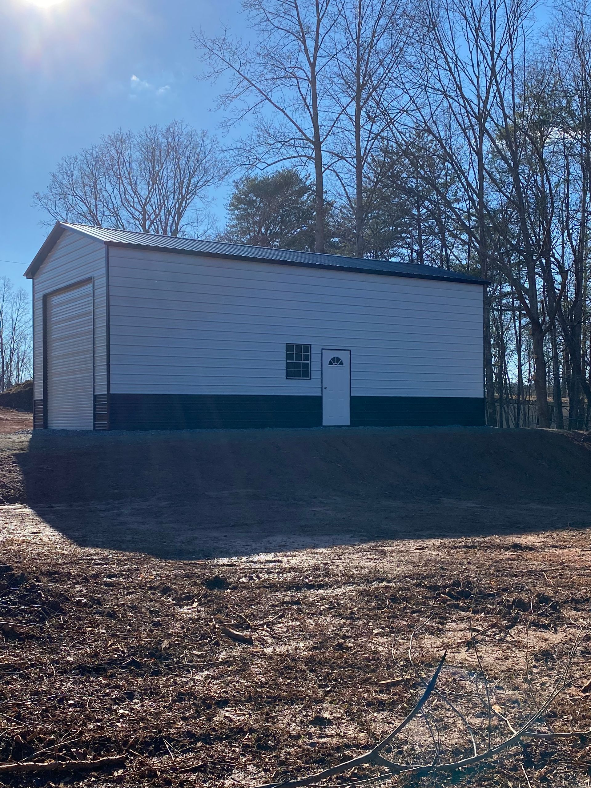 Small white utility building with a dark green base on a wooded hillside in daylight