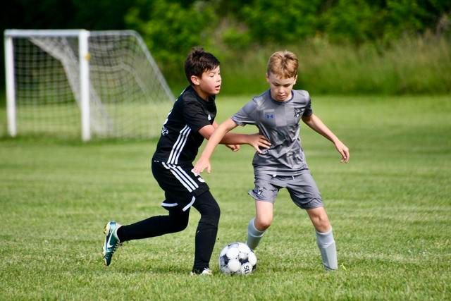 Two young soccer players in action on a green field, one dribbling the ball, the other attempting to take it.