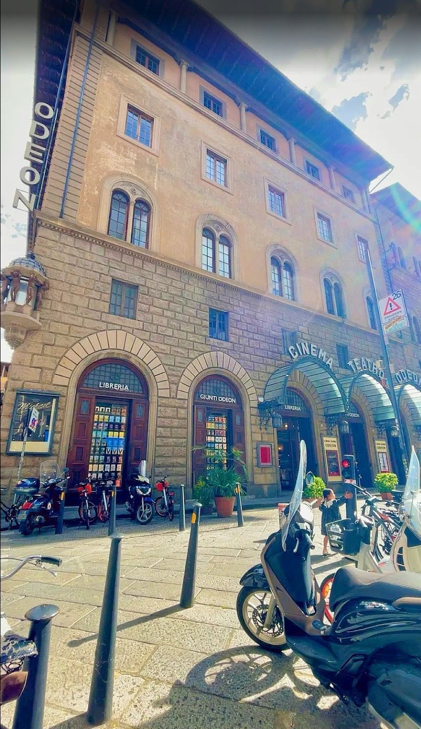 Stone building with arched storefronts and parked scooters on a sunny street corner