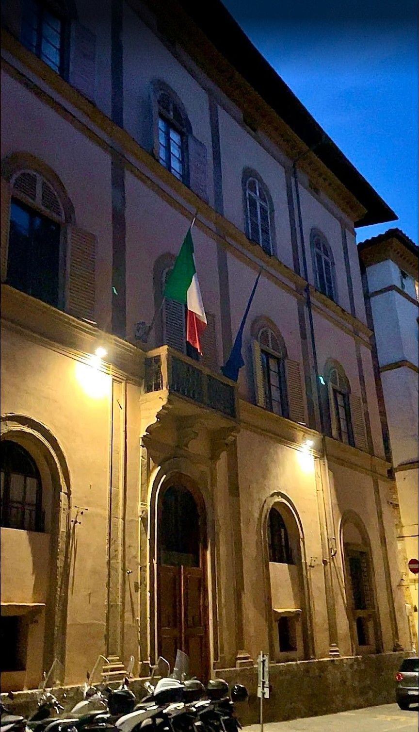 Historic building facade at dusk with arched entrances and an Italian flag hanging above the doorway