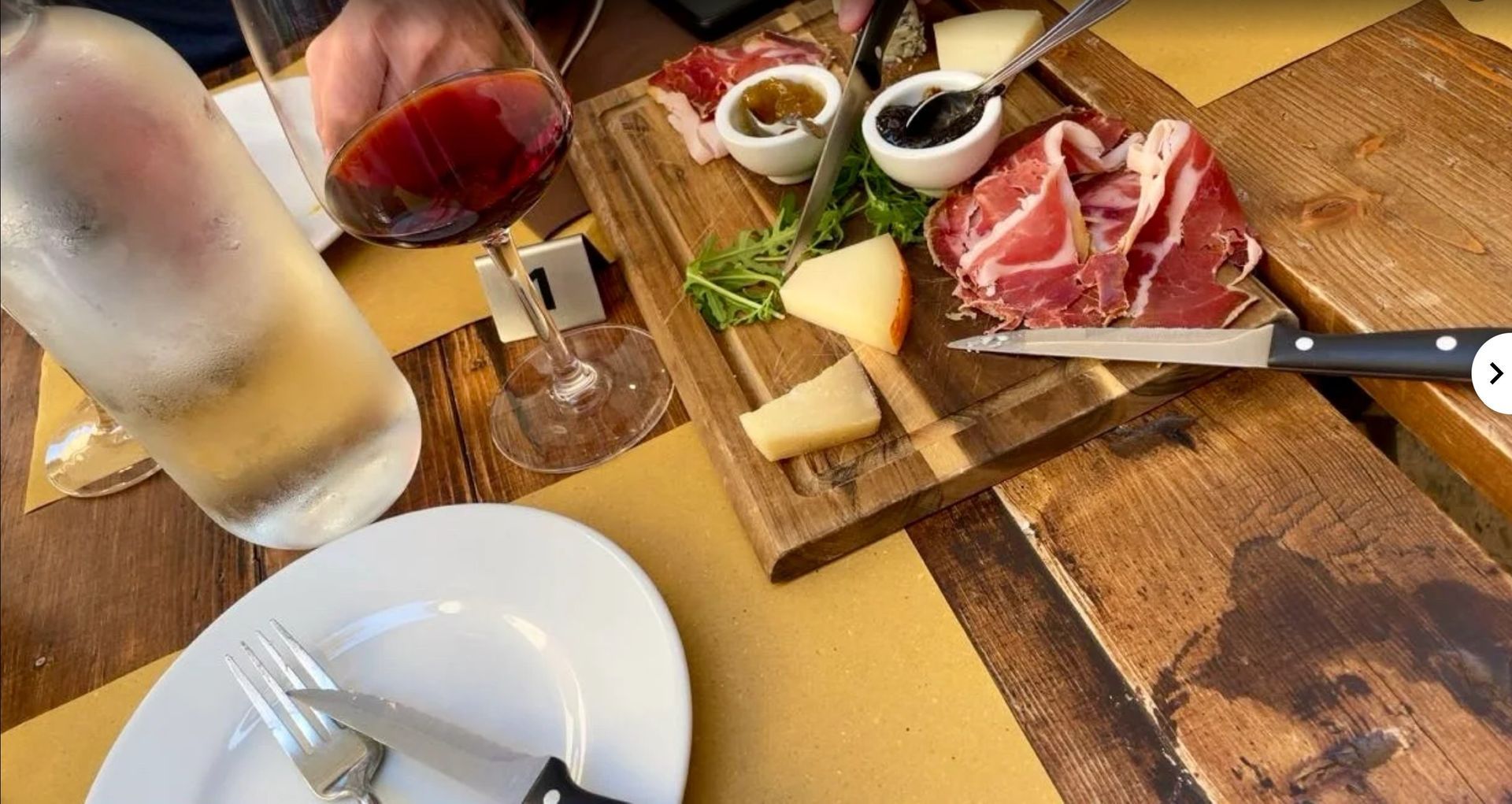 Charcuterie board with cheese, cured meats, olives, and bread beside drinks on a wooden table