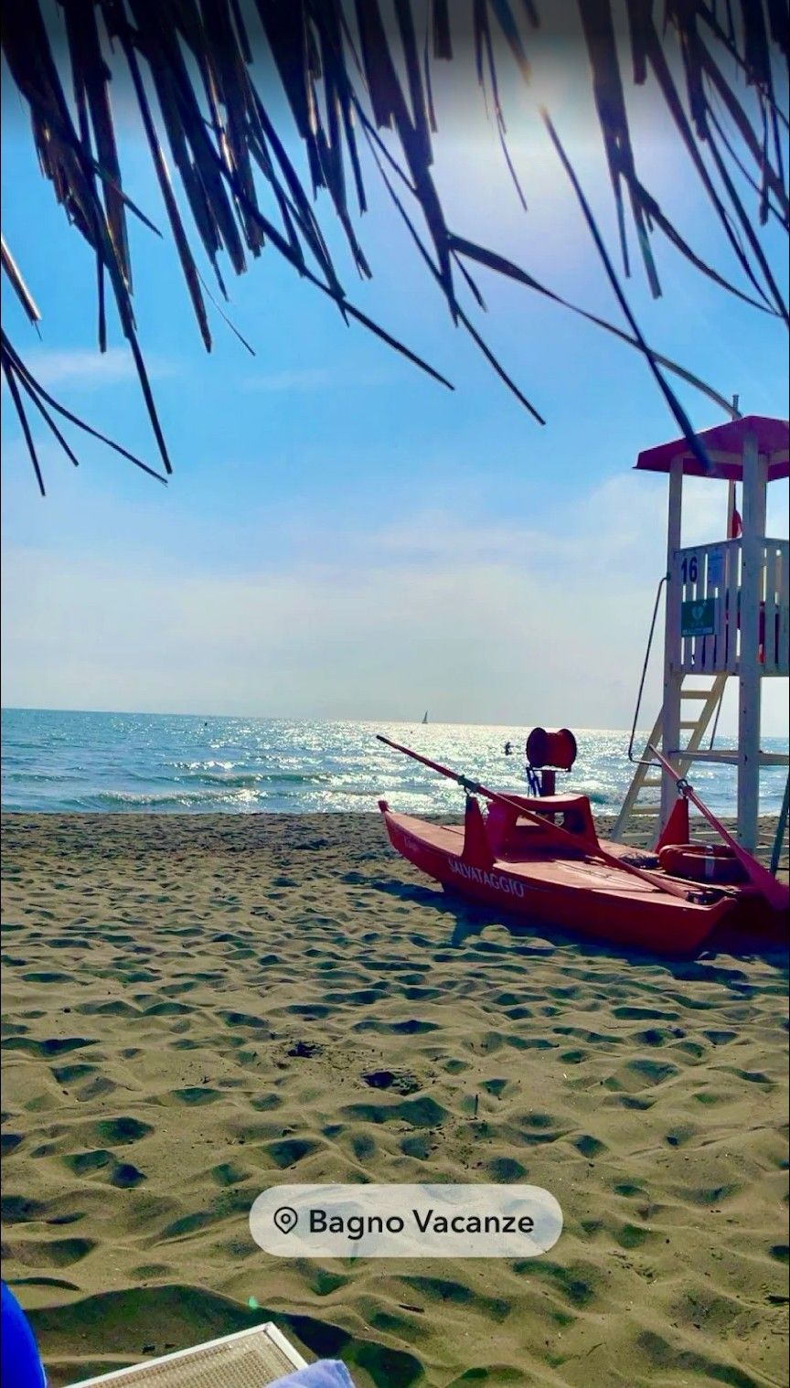 Red kayak on a sandy beach beside a lifeguard tower, with the ocean in the background.