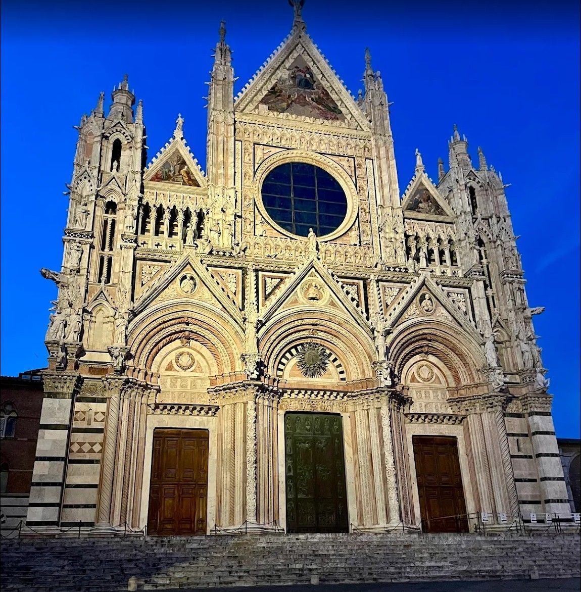 Gothic cathedral facade with rose window, three arched doorways, and twin towers against a deep blue sky