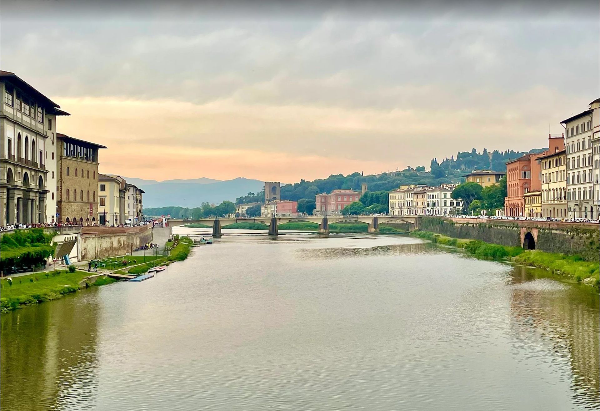 River cityscape with bridges, colorful buildings, and green hills under a cloudy sky