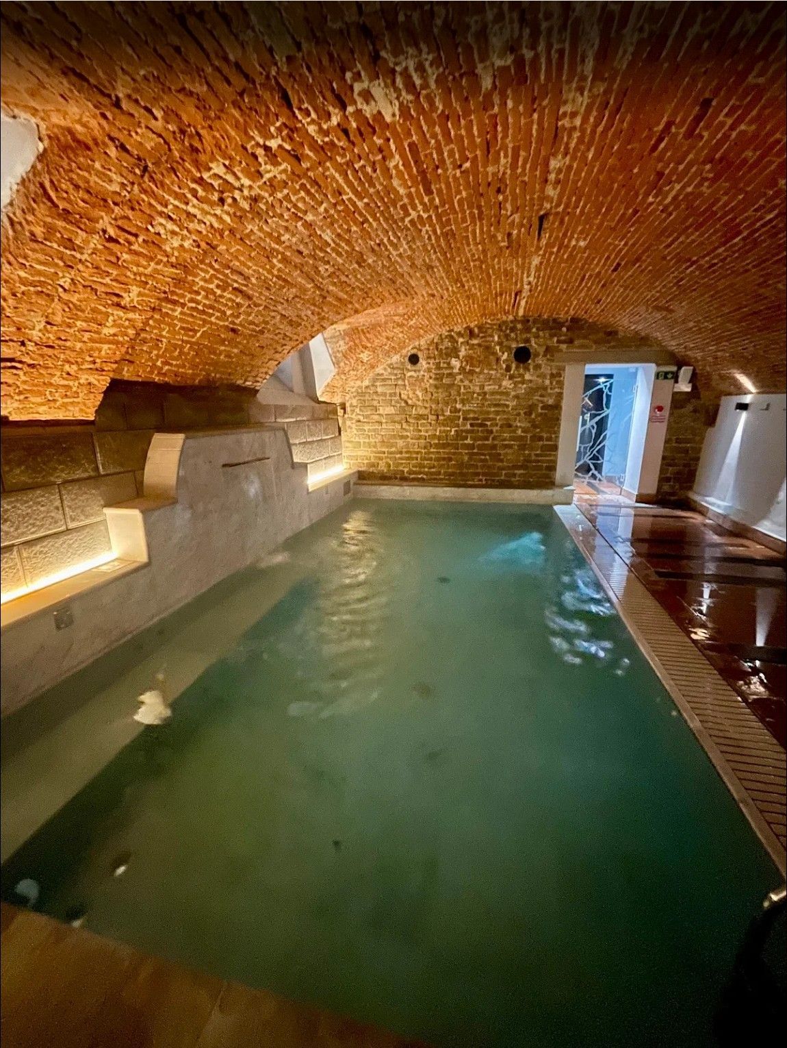 Indoor pool with green water under a brick vaulted ceiling, lit by warm lights