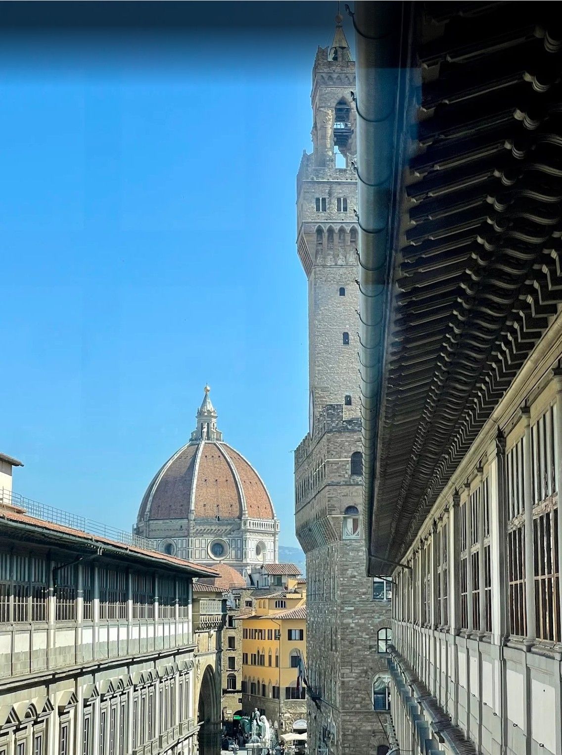 Florence skyline with Duomo dome and Palazzo Vecchio tower framed by historic buildings and blue sky