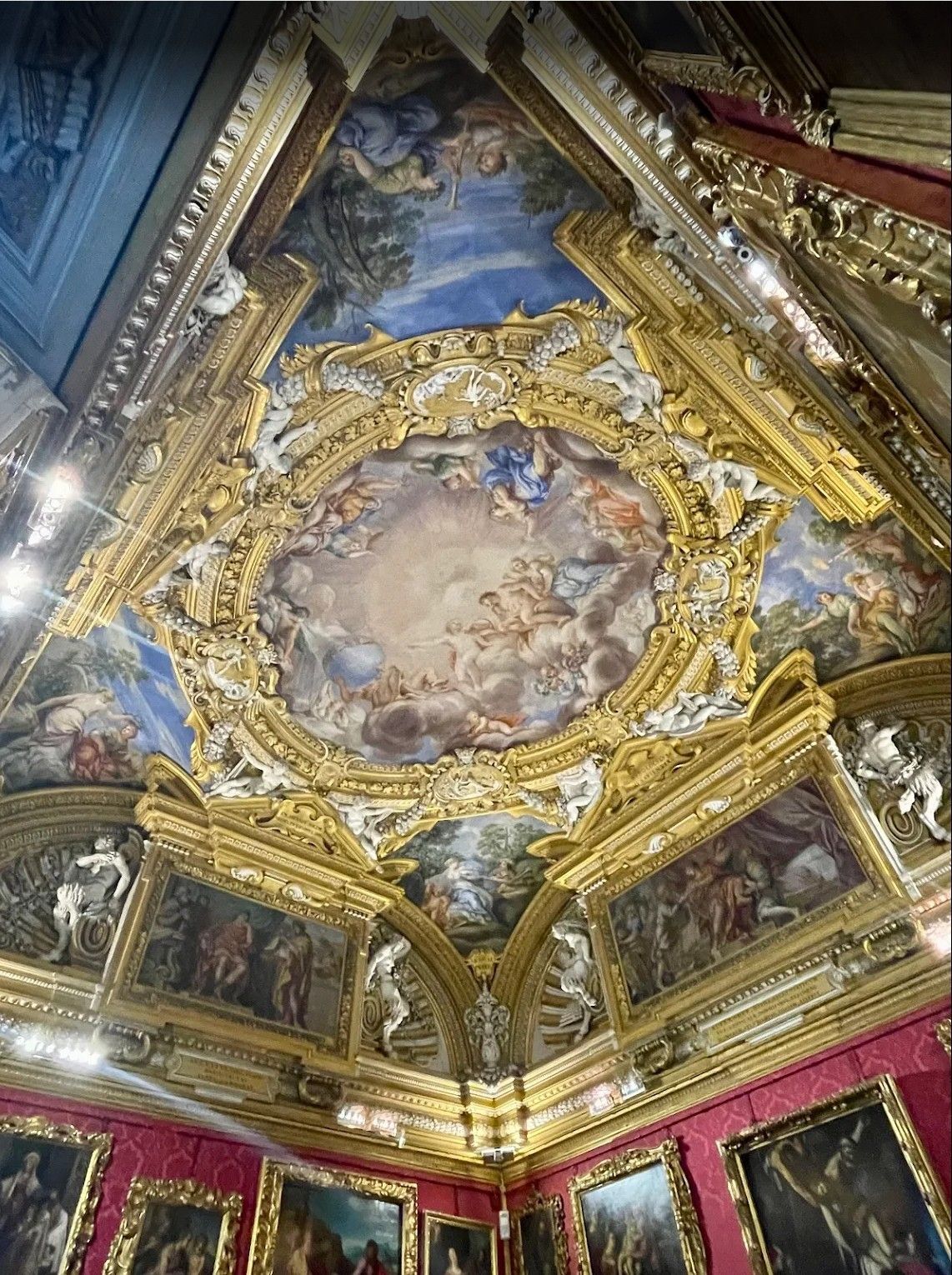 Ornate gilded ceiling fresco with painted figures and blue sky panels in a grand interior