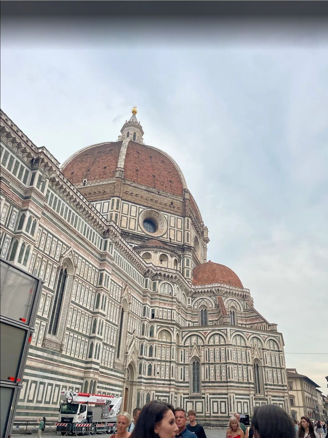 Florence Cathedral dome and facade with tourists in the foreground under a cloudy sky