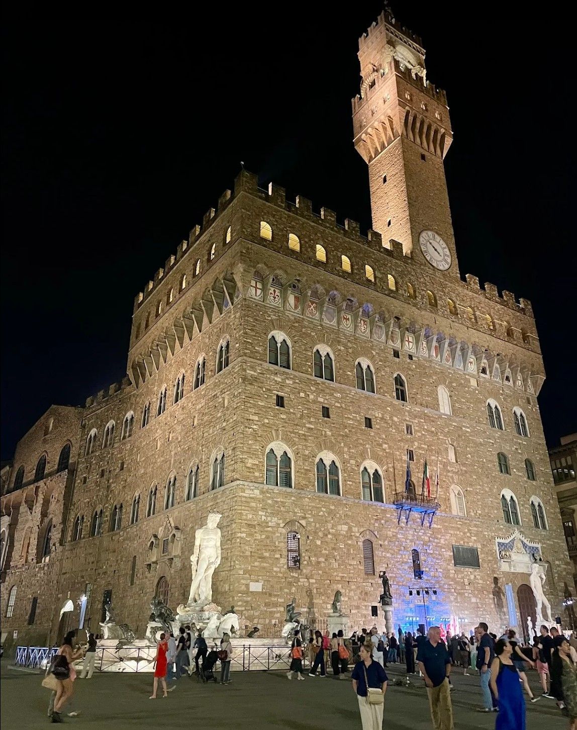 Night view of Palazzo Vecchio in Florence, lit up with crowds gathered below.