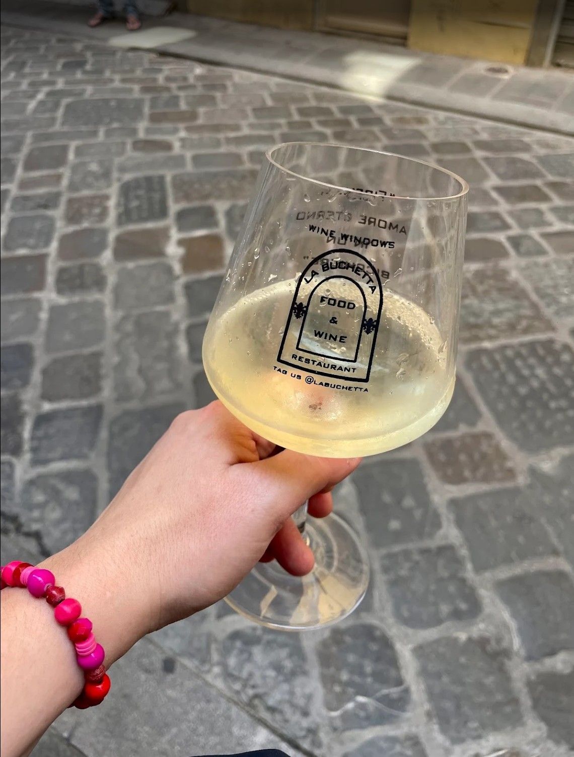 Hand holding a glass of white wine over a cobblestone street