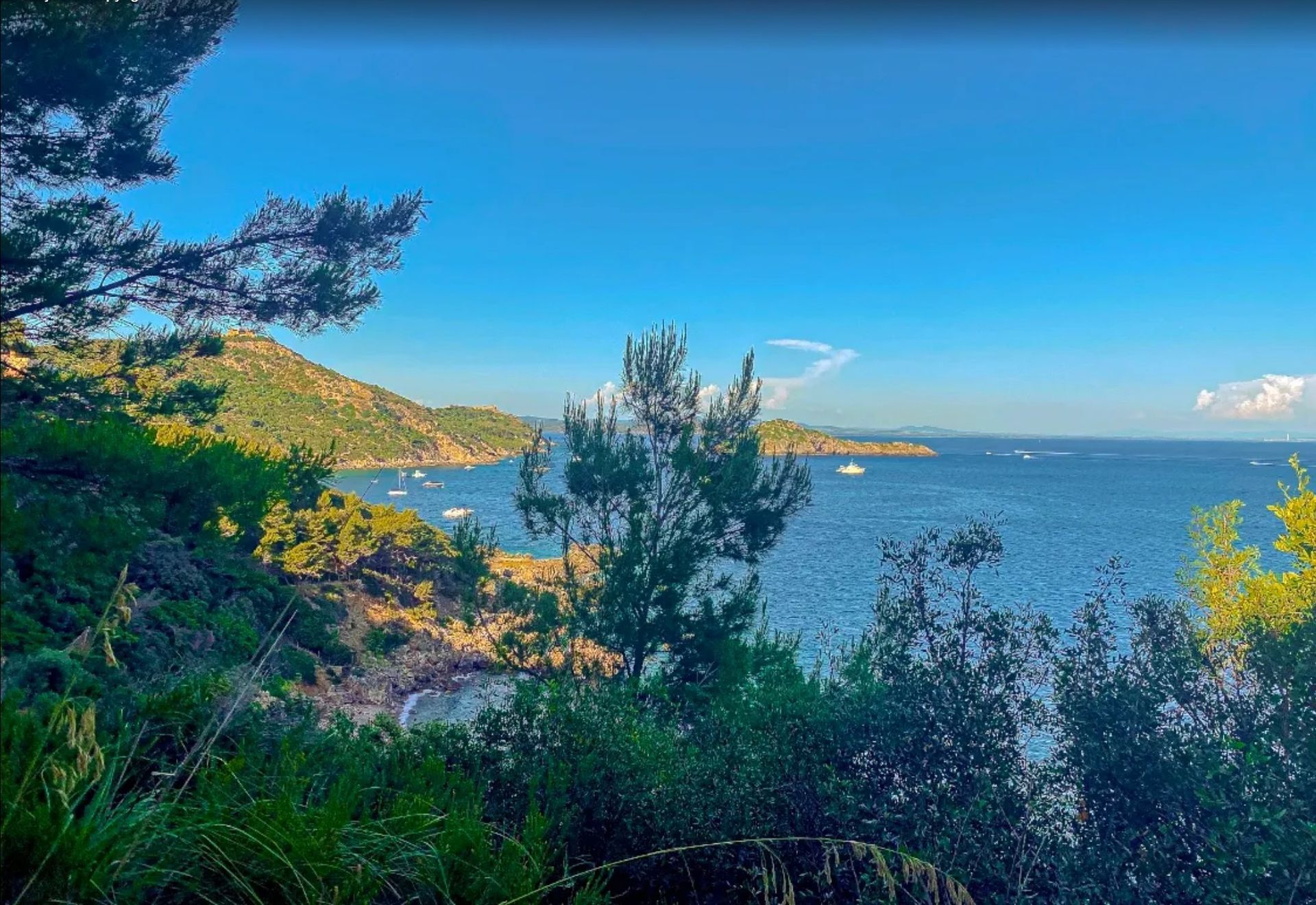 Coastal bay view with blue water, green hills, and a small boat under a clear sky