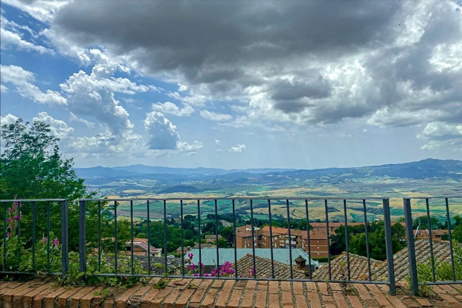 Panoramic city view from a hilltop balcony under dramatic cloudy skies, with railing and brick foreground