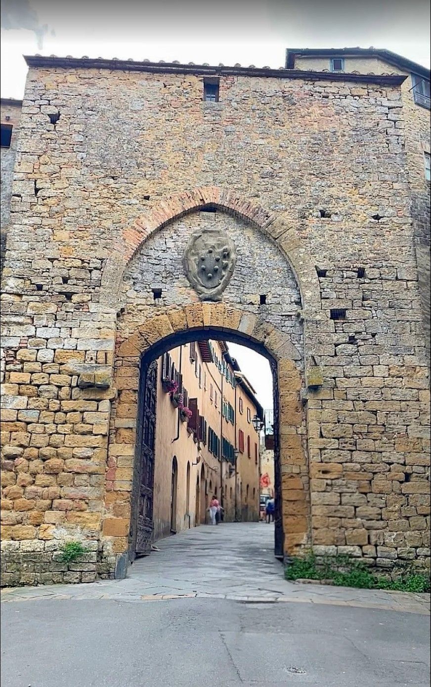 Stone archway in an old city wall framing a narrow street with buildings beyond