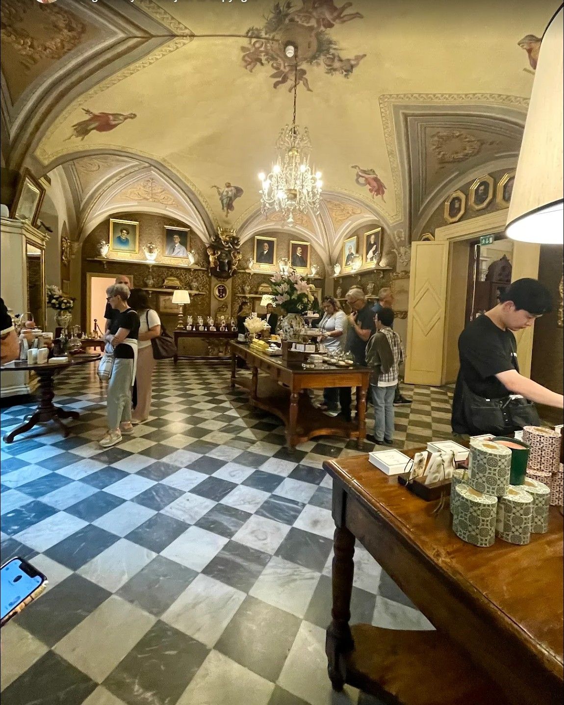 Elegant café with ornate arched ceiling, black-and-white tiled floor, and people seated at tables