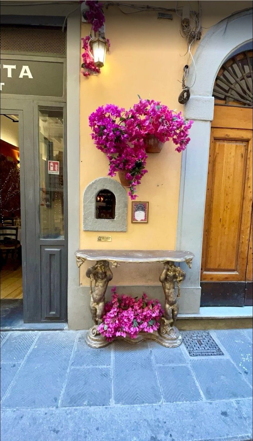 Street wall with mailbox, wooden door, and bright pink flowers in a narrow stone alley