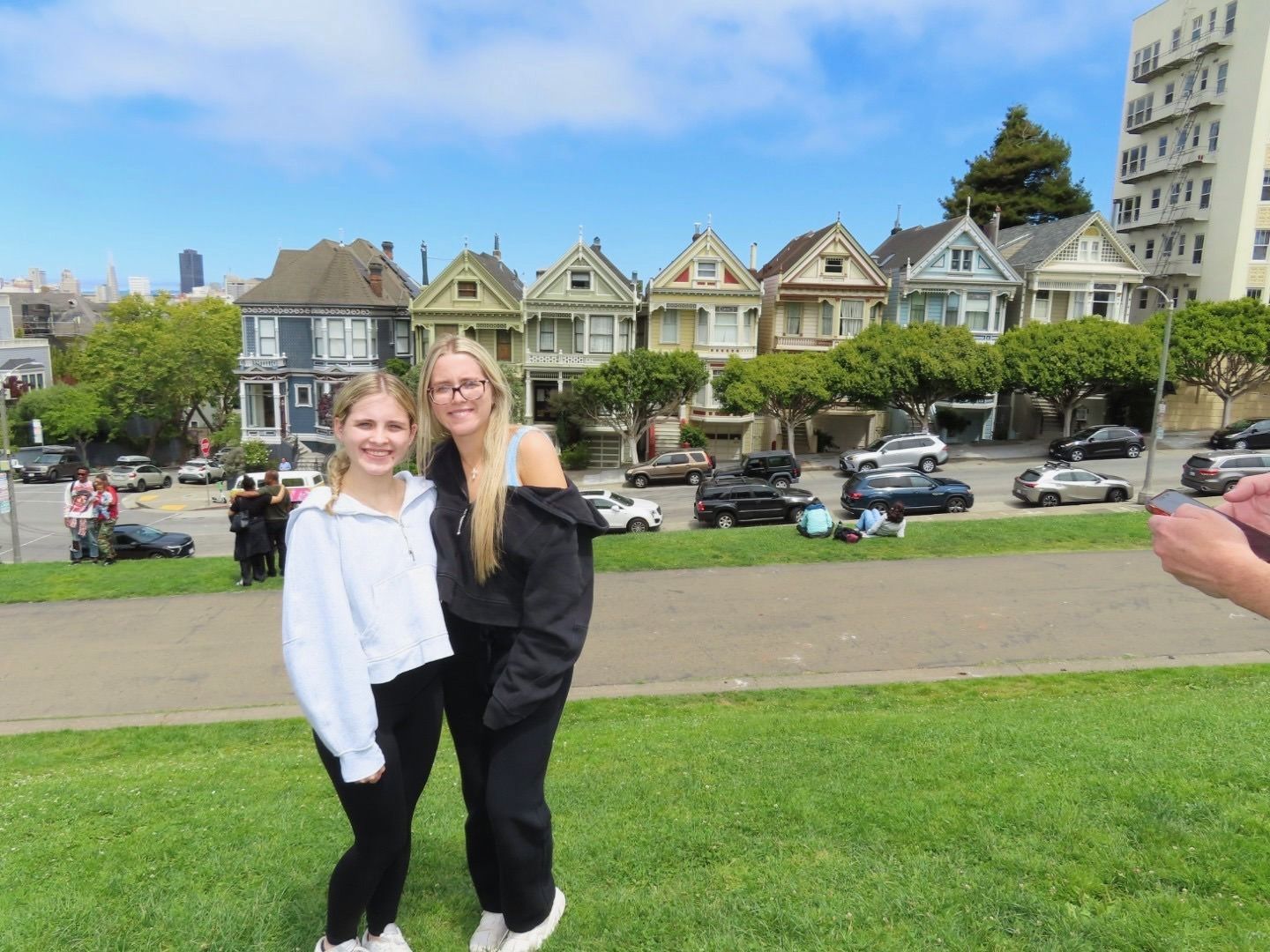 Two people posing on a grassy hill with Victorian houses and a city skyline behind them