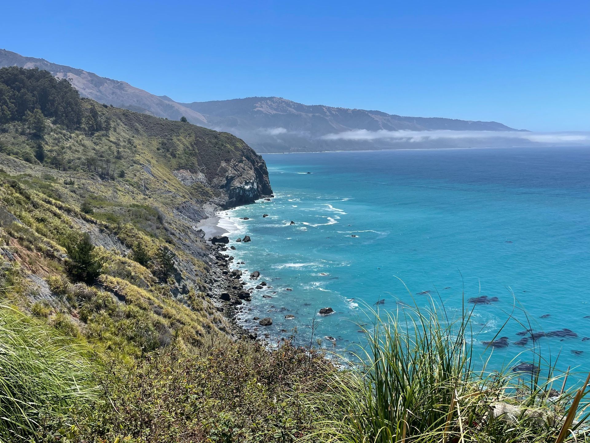 Rocky coastal cliffs overlooking turquoise ocean and distant mountains under a clear blue sky