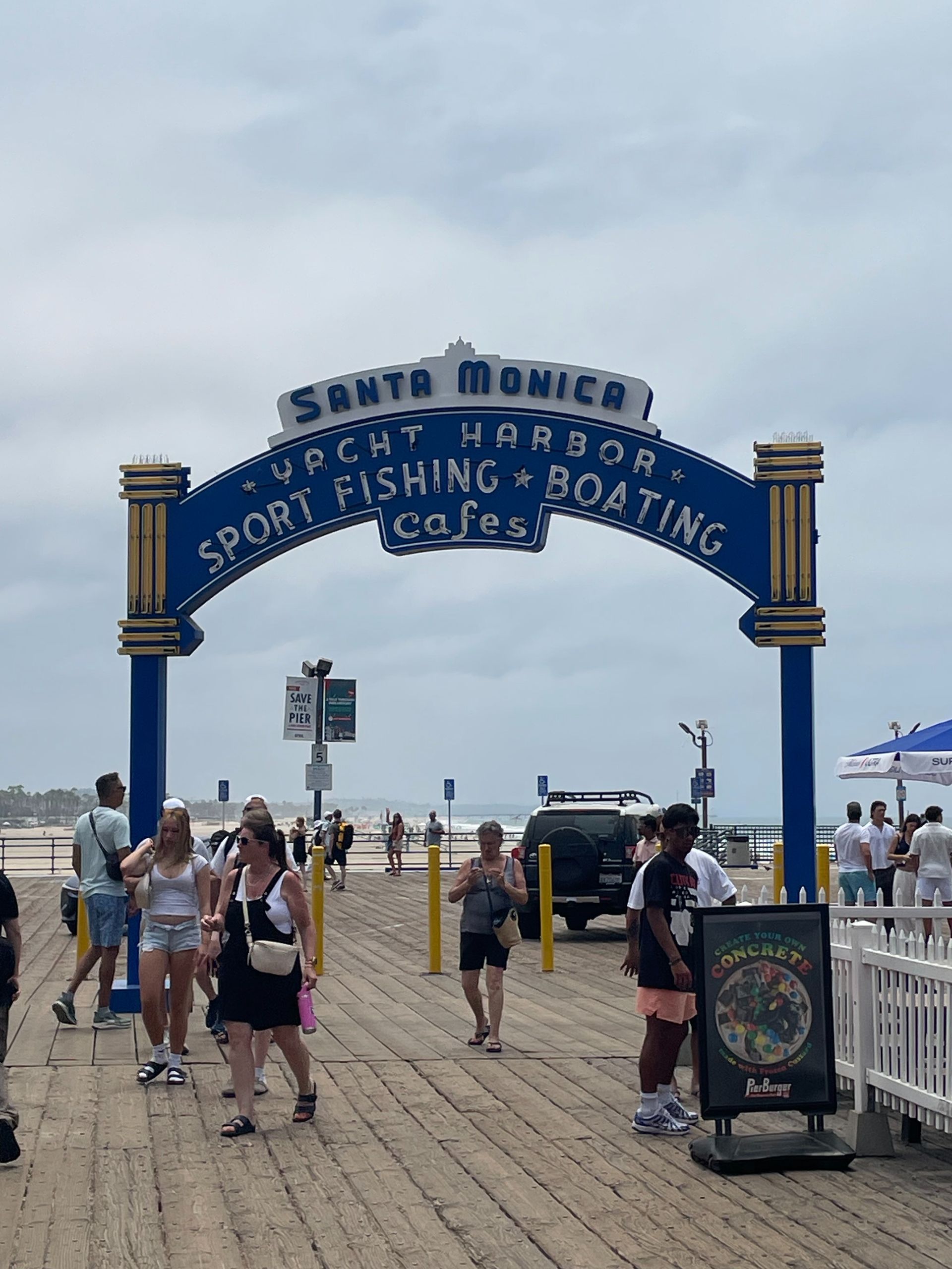 Santa Monica Pier arch over crowded wooden boardwalk on a cloudy day