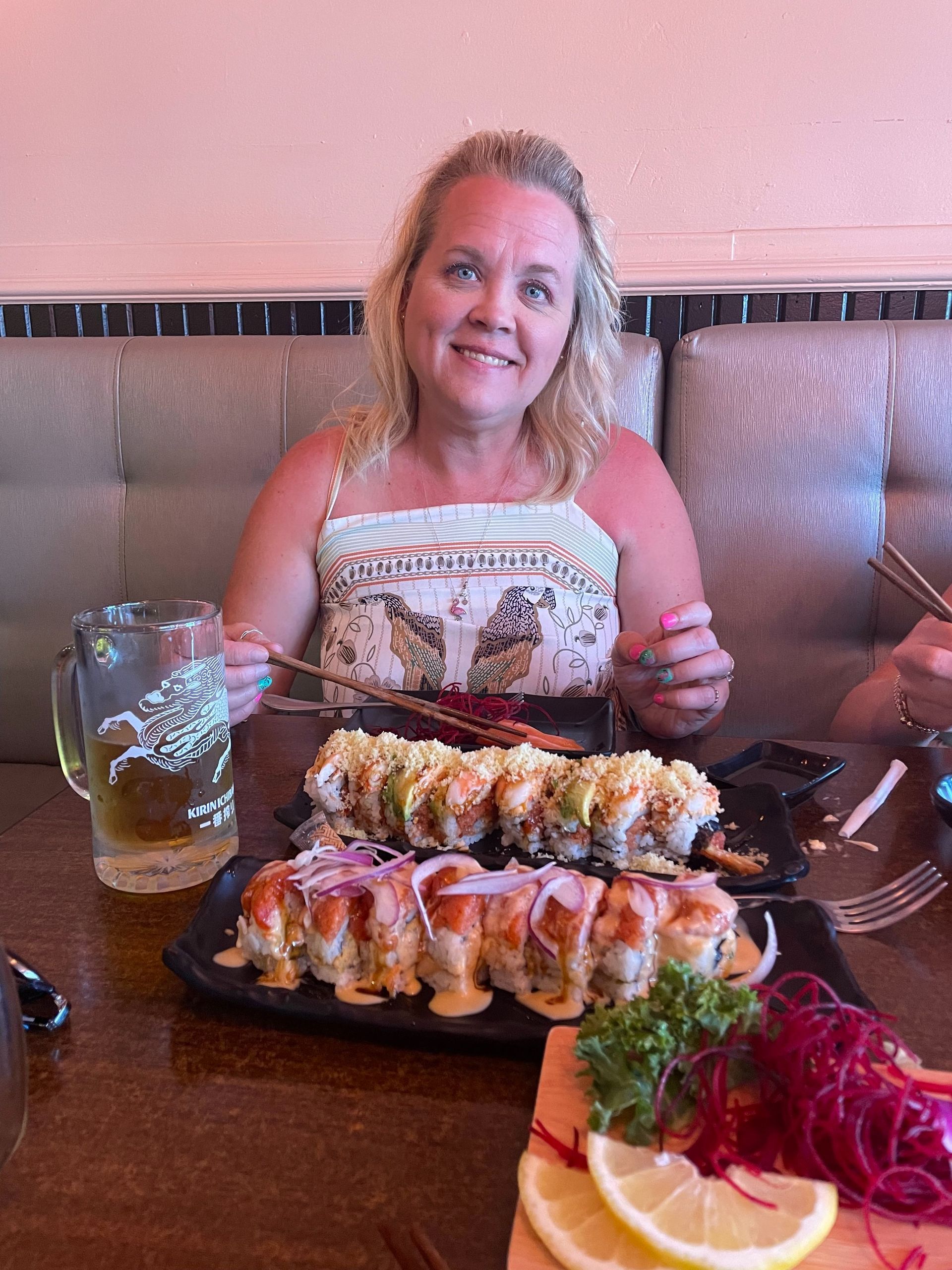 Woman at a restaurant table with a large sushi platter, smiling and holding chopsticks.