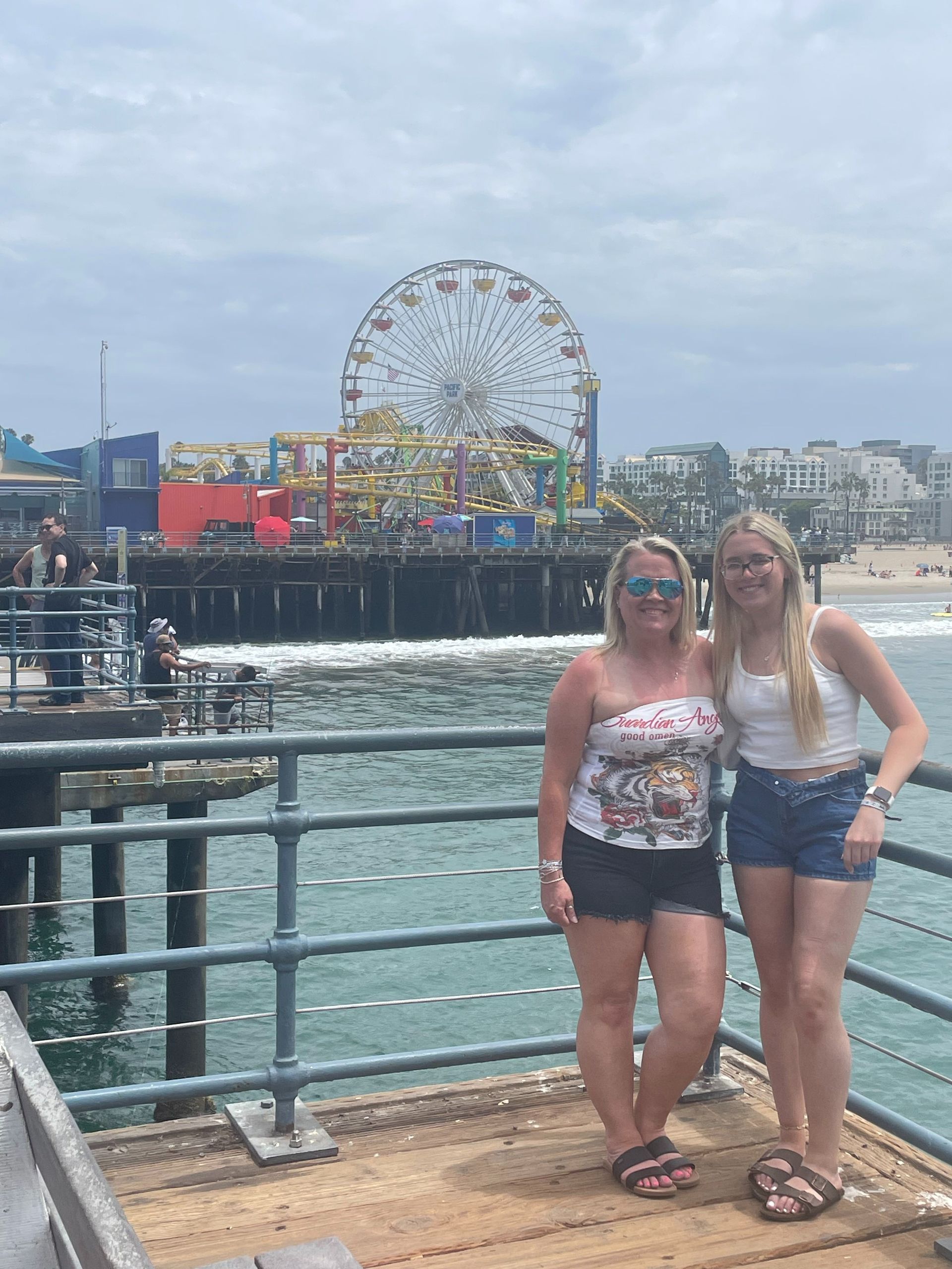 Two women standing on a pier with a Ferris wheel and fairground in the background