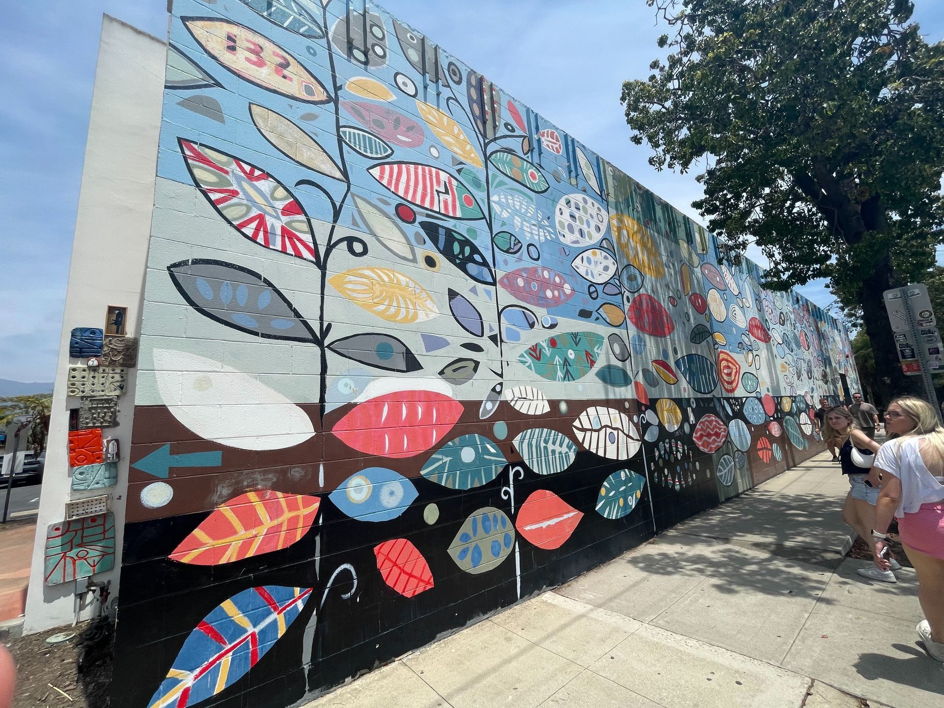 Colorful fish mural on a long wall beside a sidewalk, with a few people walking nearby.