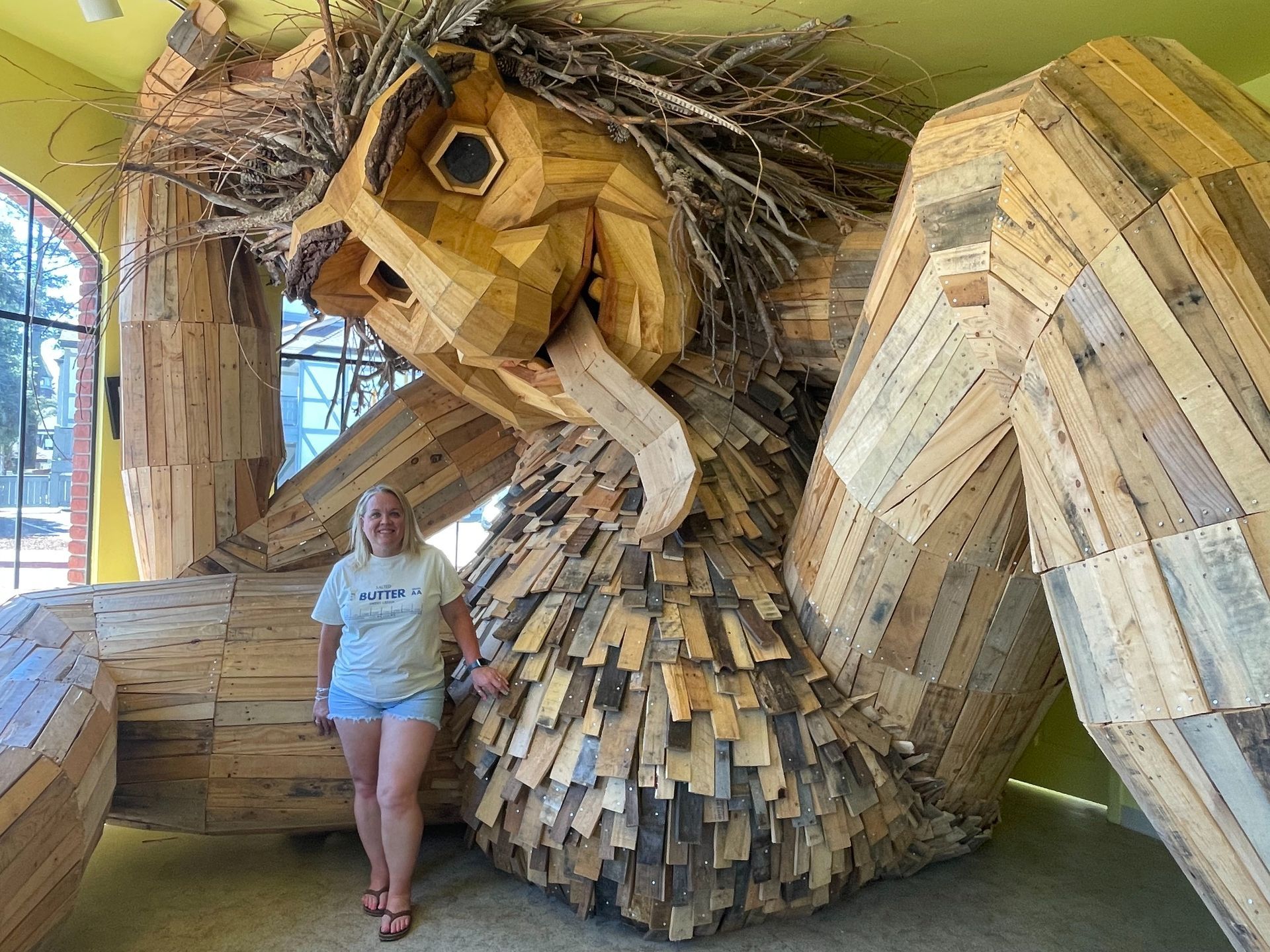 Woman posing beside a giant wooden sculpture in a gallery.